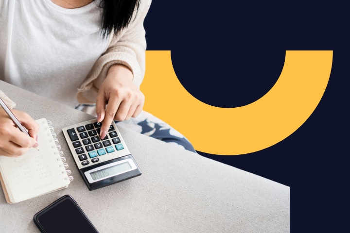 Osoba píše do zápisníku a používá kalkulačku, vedle je položený mobil