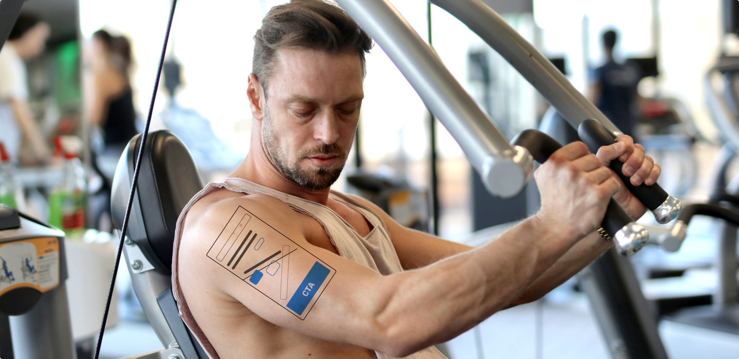 Muž cvičí v posilovně na stroji a má na rameni tetování připomínající uživatelské rozhraní s tlačítkem CTA.