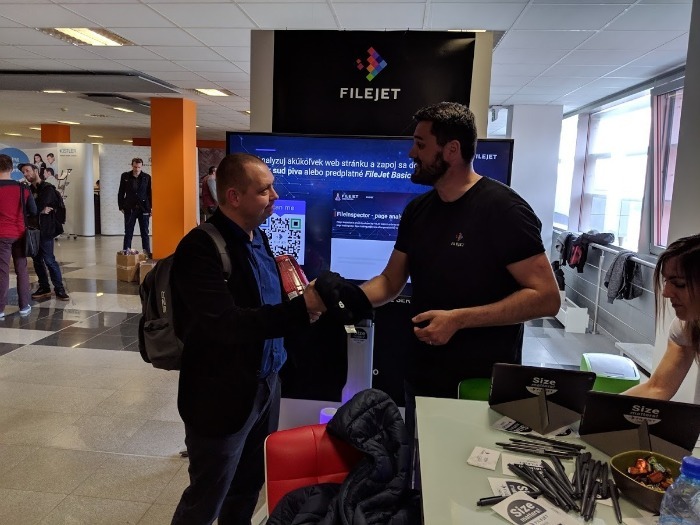 Dvě osoby si podávají ruce na stánku FileJet během konference.