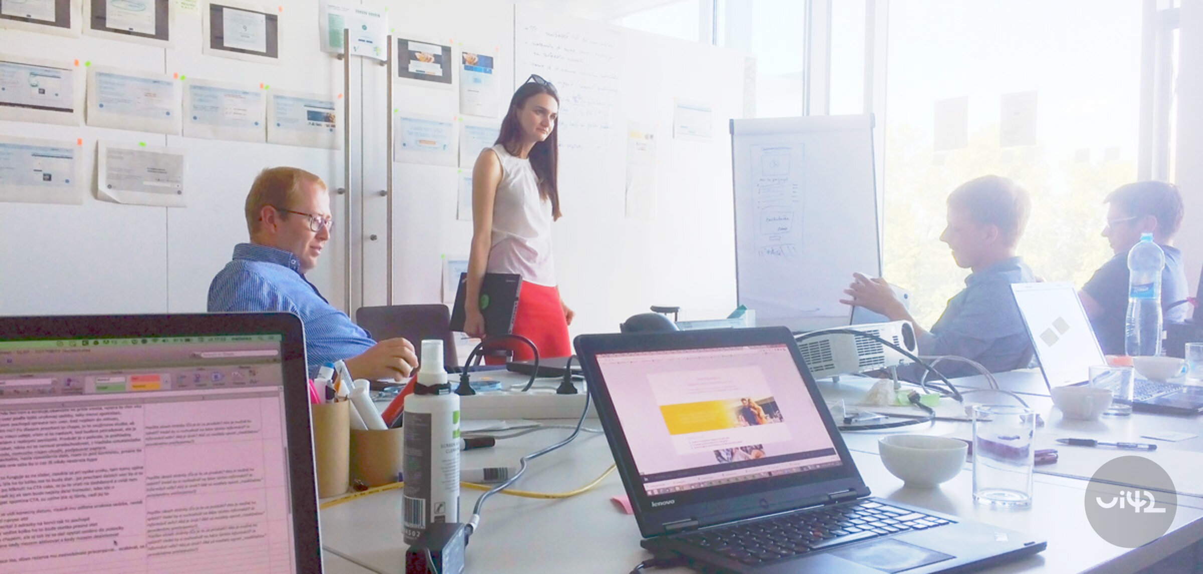 Týmová diskuse u stolu s notebooky a nástěnkou v kanceláři