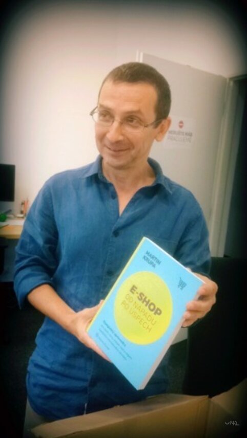 Muž v modré košili drží knihu s názvem 'E-SHOP OD NÁPADU PO ÚSPĚCH'