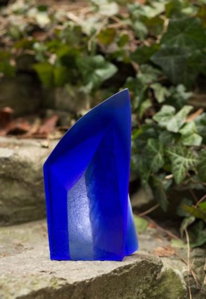 Modrá skleněná socha na kamenném pozadí s listy břečťanu.