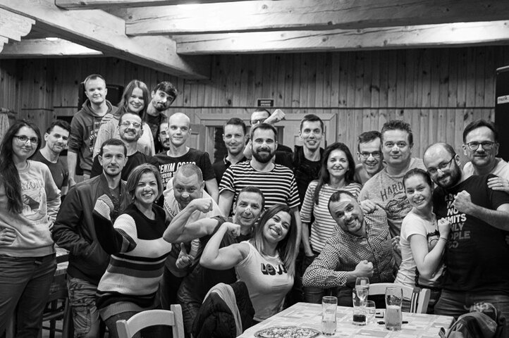 Skupinová fotografie veselých lidí oslavujících spolu v interiéru s dřevěnými stěnami.