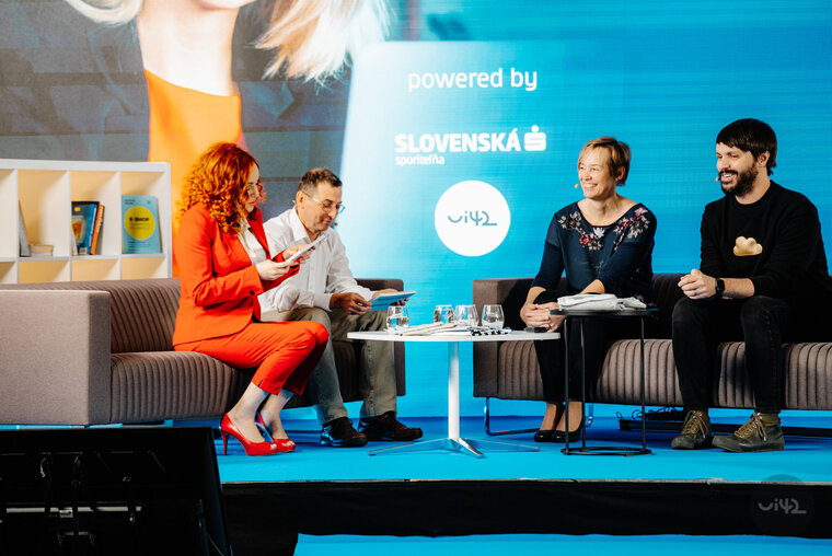Diskuse na online konferenci se čtyřmi účastníky sedícími na pódiu. Žena v červeném kostýmu čte z tabletu, vedle ní muž v bílé košili, žena v tmavomodré blůze a muž v černém svetru. Na pozadí logo Slovenské spořitelny.
