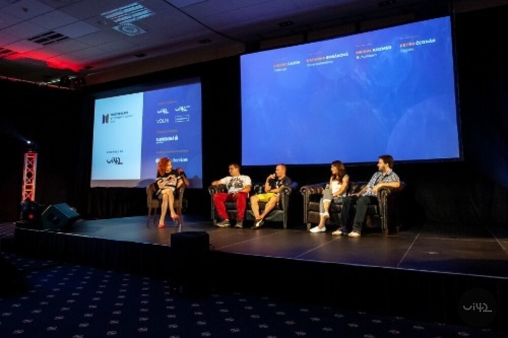 Diskuse na pódiu během konference MastersGate, kde pět účastníků sedí na křeslech před velkou obrazovkou.