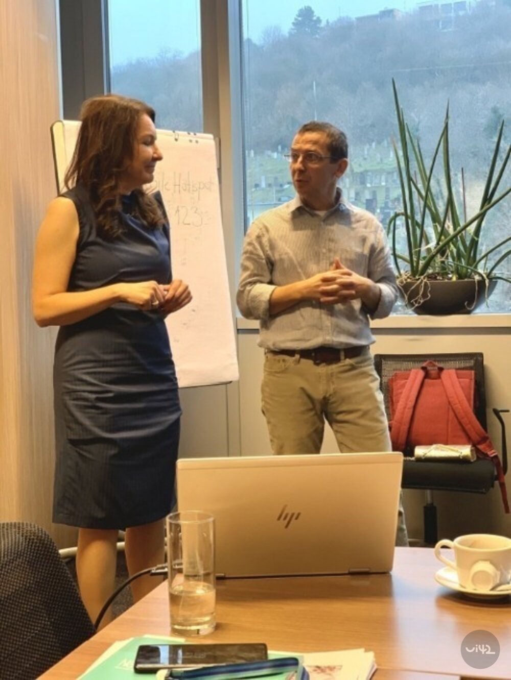 Dvě osoby diskutující v kanceláři u stolku s notebookem a kávou.