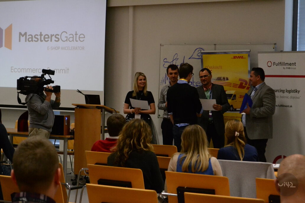 Úspěšný MastersGate E-commerce Summit, účastníci přijímají ocenění, kameraman nahrává událost, prezentace na plátně.