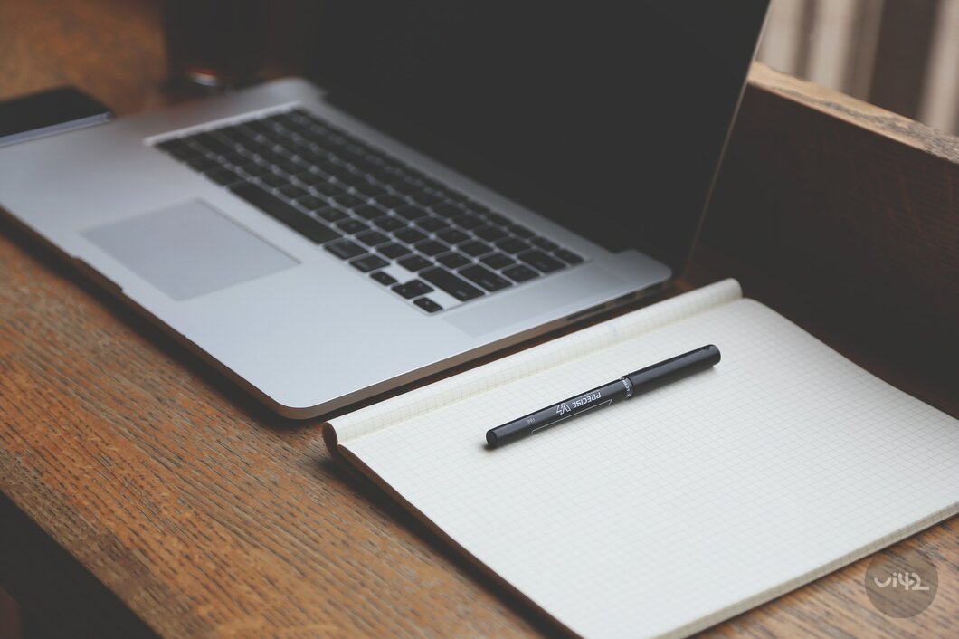 Notebook a pero na stole vedle otevřeného notebooku