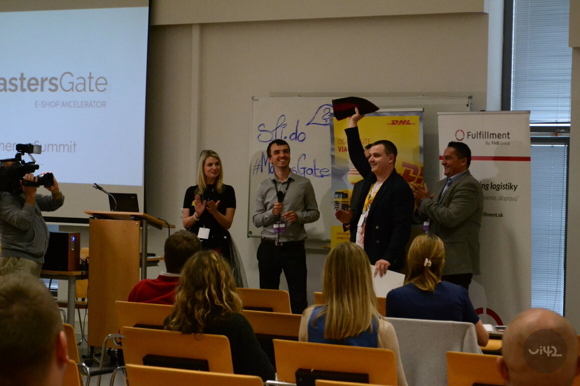 Lidé na pódiu během MastersGate E-commerce Summit, kamera natáčí, publikum sedí v hledišti.