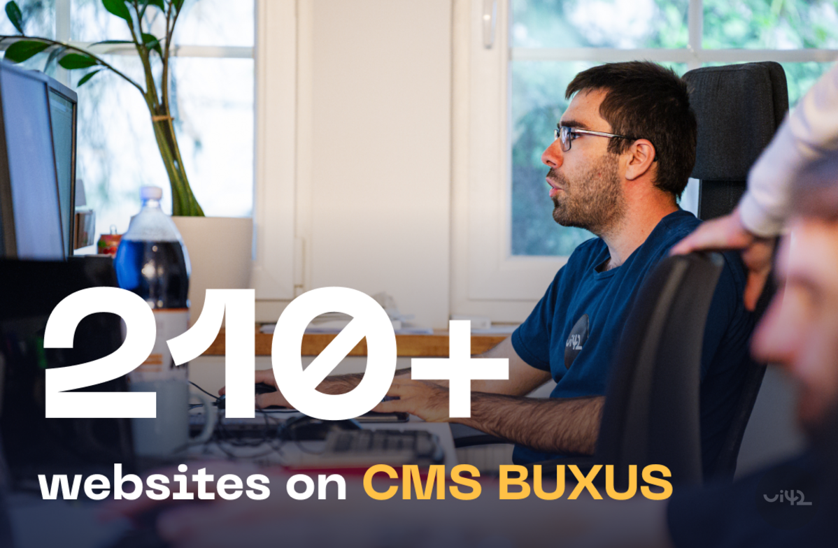 Muž pracující na počítači v kanceláři s nápisem '210+ websites on CMS BUXUS'.