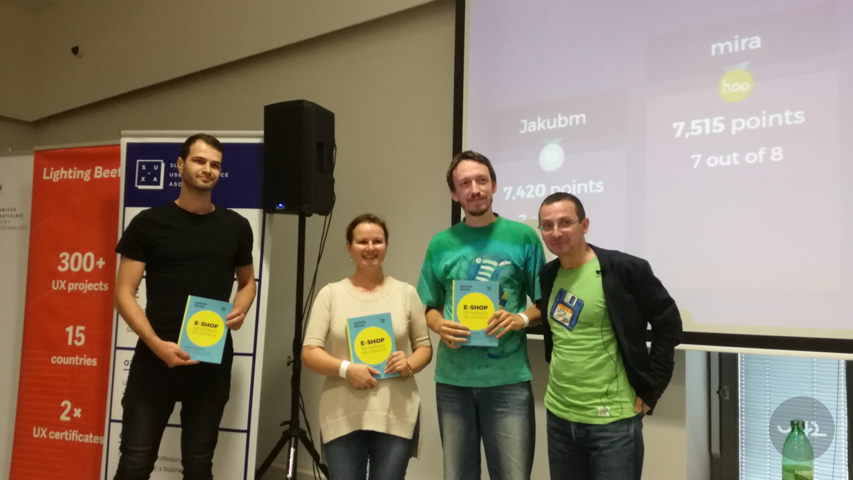 Skupina lidí na akci WUD 2018 drží certifikáty a stojí před projektorem s výsledky soutěže.