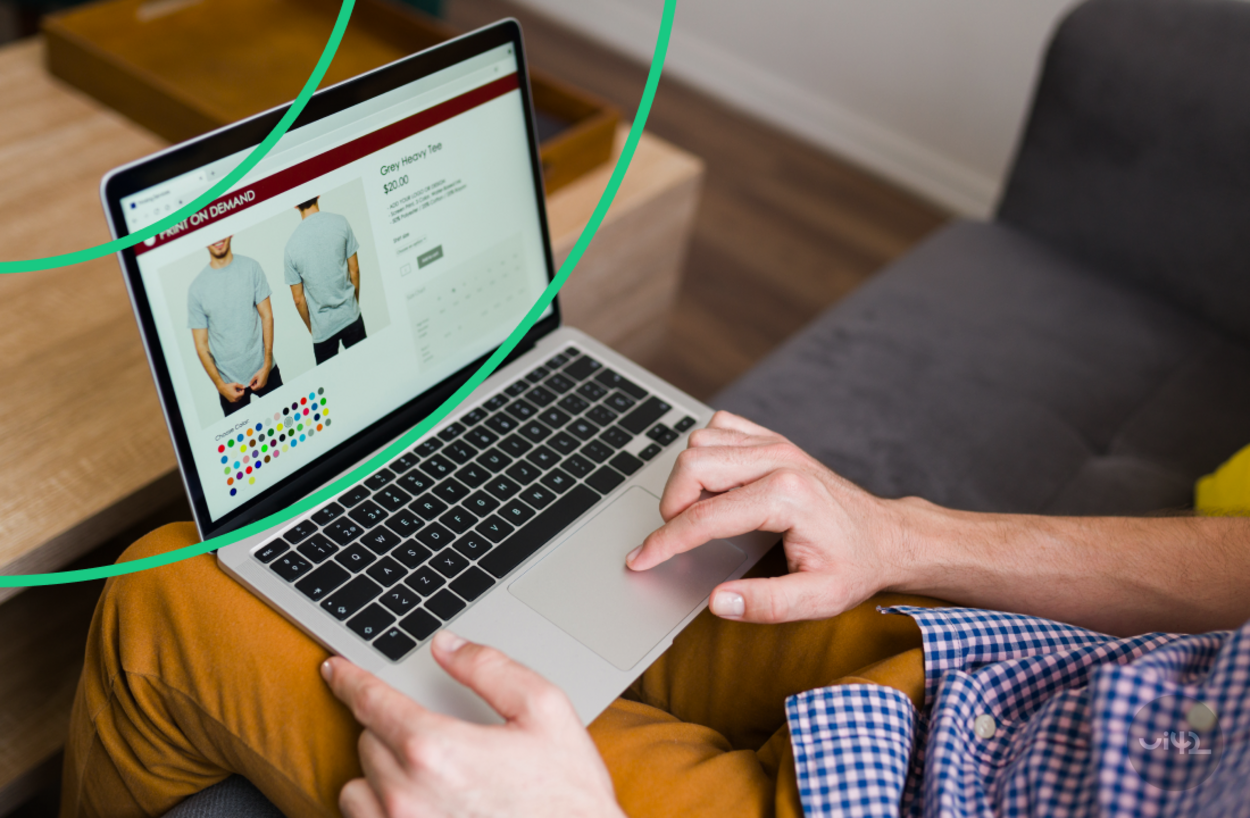 Muž sedí na pohovce a nakupuje oblečení online na notebooku. Na obrazovce je zobrazené tričko s různými barevnými možnostmi.