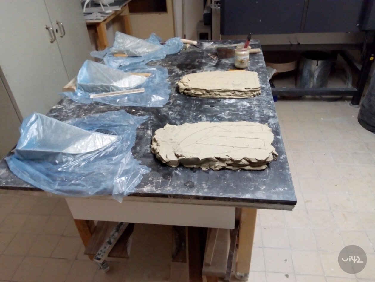 Příprava hliněných trofejí na pracovním stole s modrými plastovými fóliemi a nářadím.