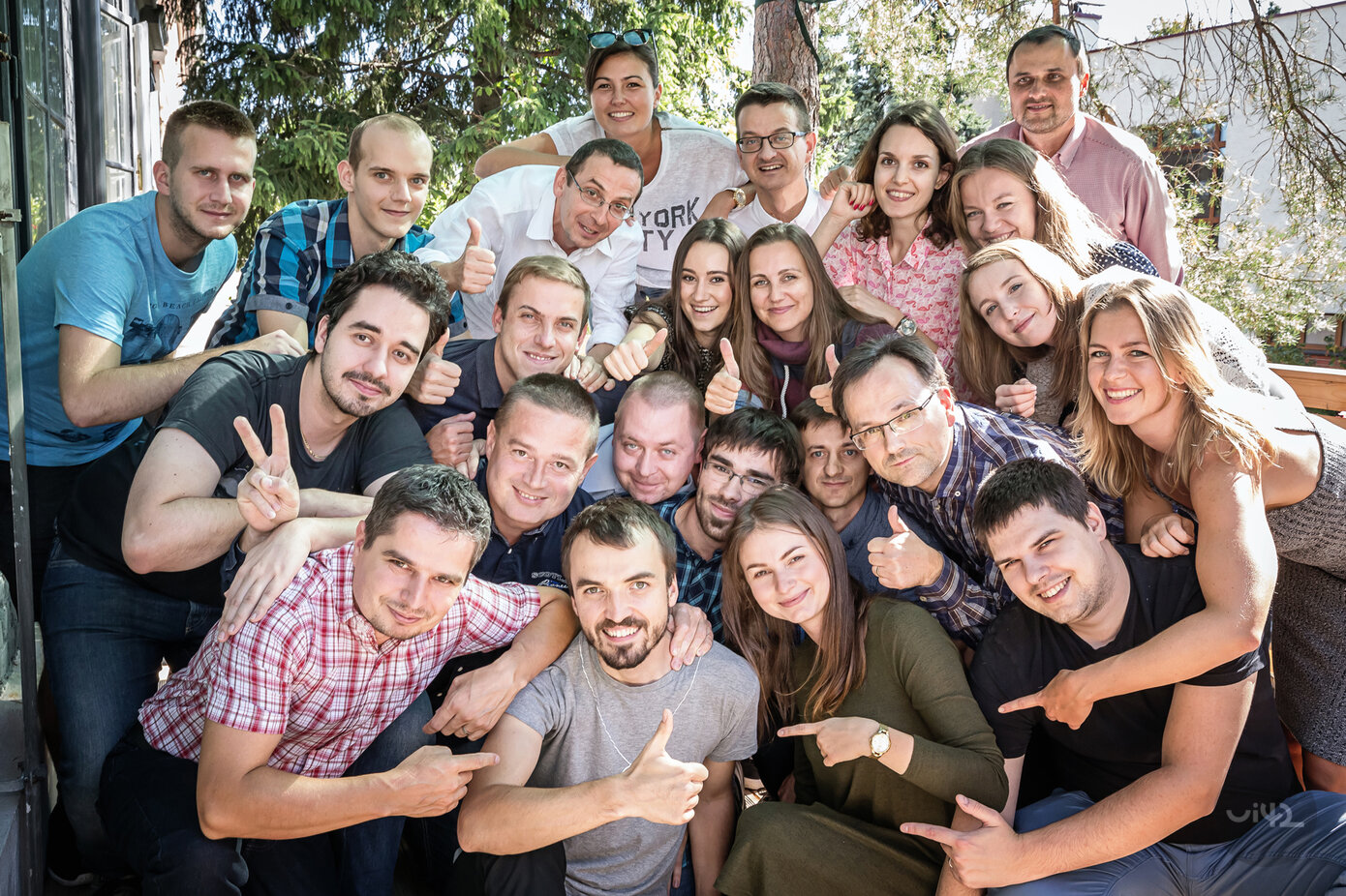 Skupinová fotografie lidí na zahradě, všichni se usmívají a ukazují palce nahoru.