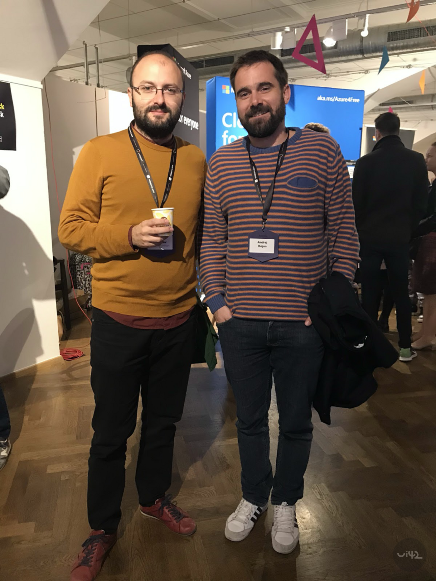 Dva muži na konferenci WebExpo 2019, jeden se sklenicí v ruce, oba mají jmenovky a stojí na výstavní ploše.