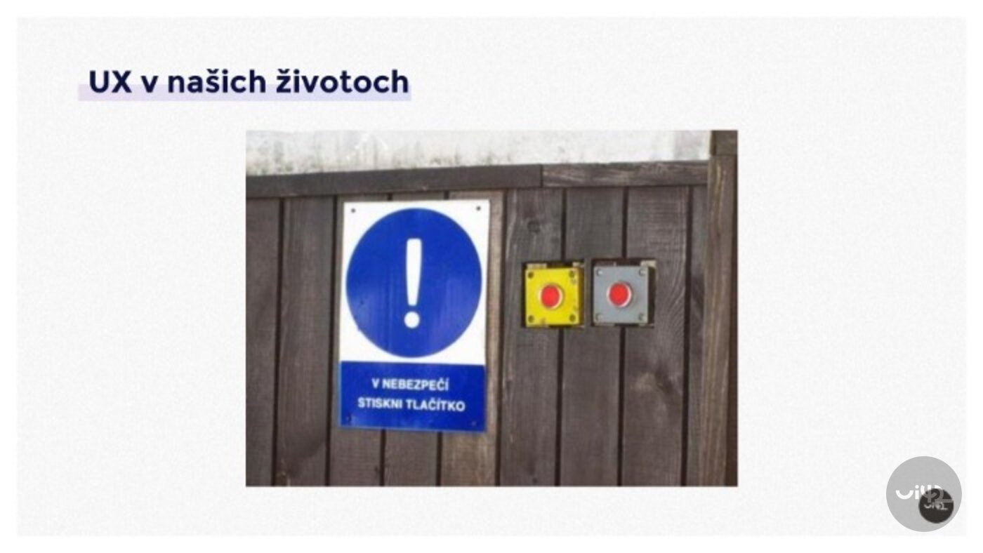 Dva nouzové tlačítka na dřevěné stěně s modrou značkou s vykřičníkem a textem 'V nebezpečí stiskni tlačítko'.