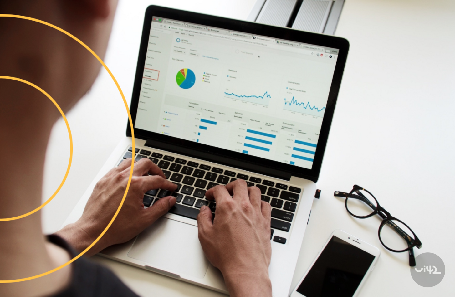 Muž pracující na notebooku se zobrazenými grafy a statistikami na obrazovce, vedle jsou položené brýle a mobilní telefon.
