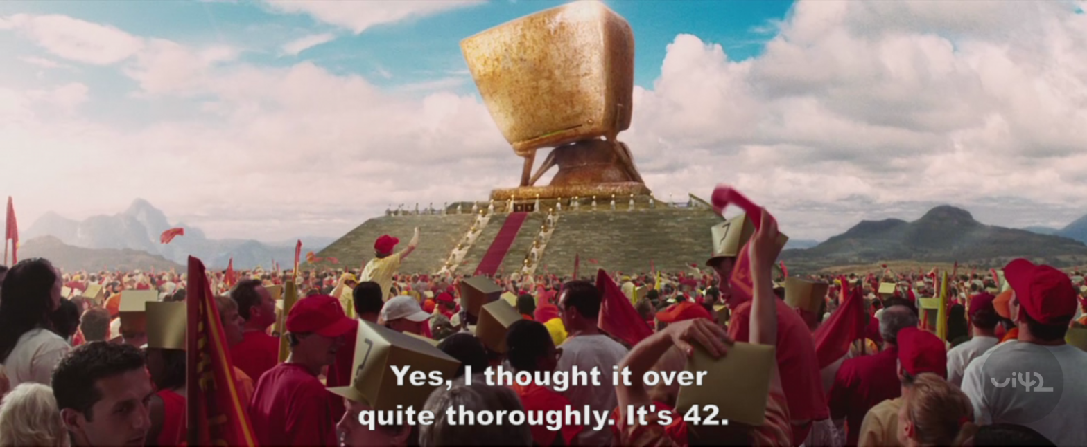 Dav lidí před velkou zlatou sochou ve tvaru poháru s titulky: 'Ano, přemýšlel jsem o tom docela důkladně. Je to 42.'