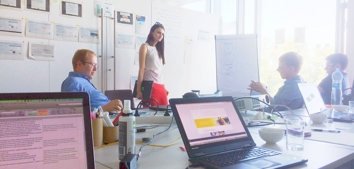 Týmová diskuse u stolu s notebooky a nástěnkou v kanceláři